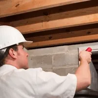 Termite inspection technician checking a basement wall and framing for termite activity in Kansas City, KS